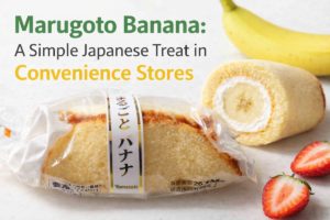 Marugoto Banana cake in its package and a cut piece showing banana and cream inside, with bananas and strawberries, introducing a Japanese convenience store dessert.